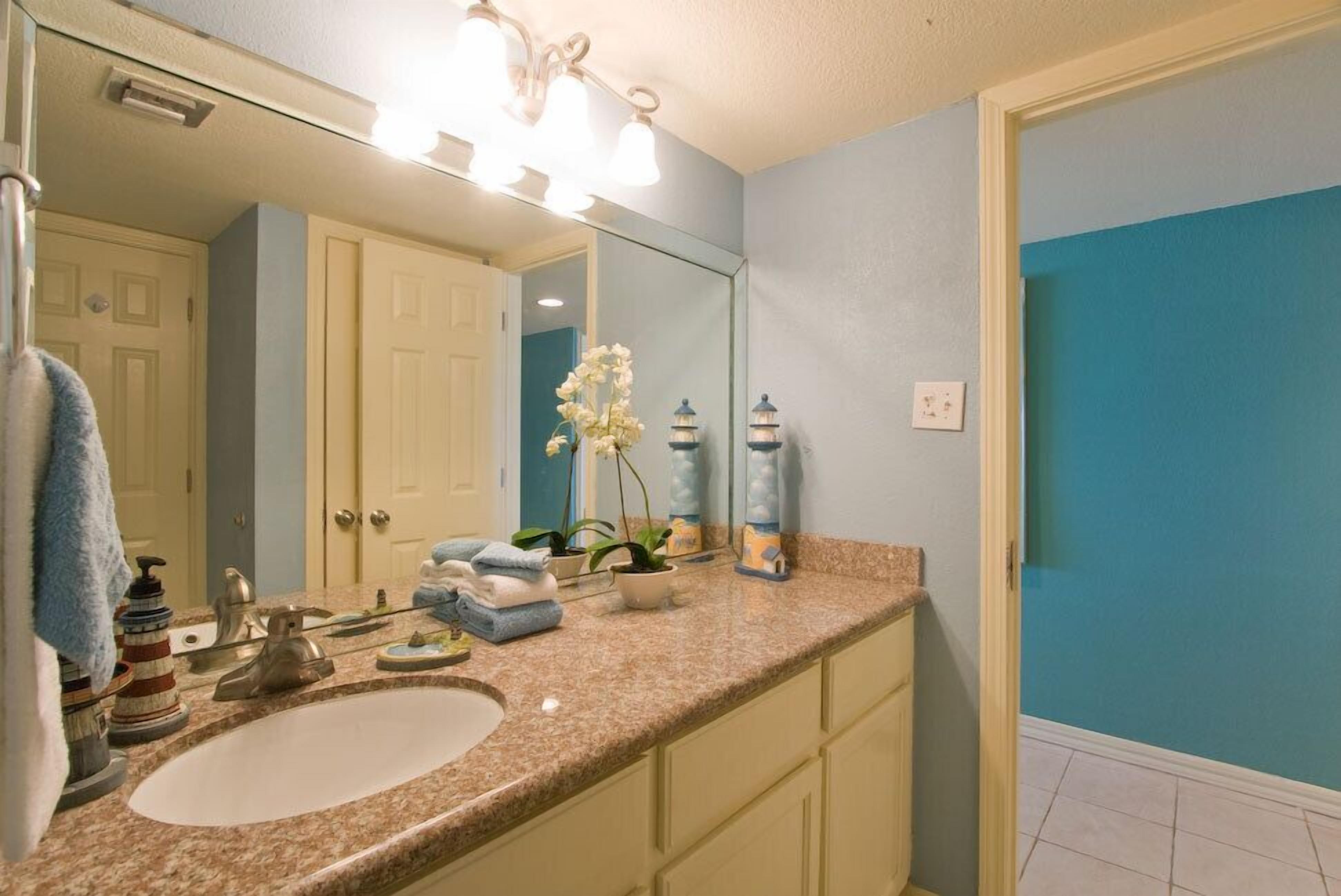 Une salle de bain avec un comptoir en granit, un lavabo blanc, un miroir et un mur bleu.