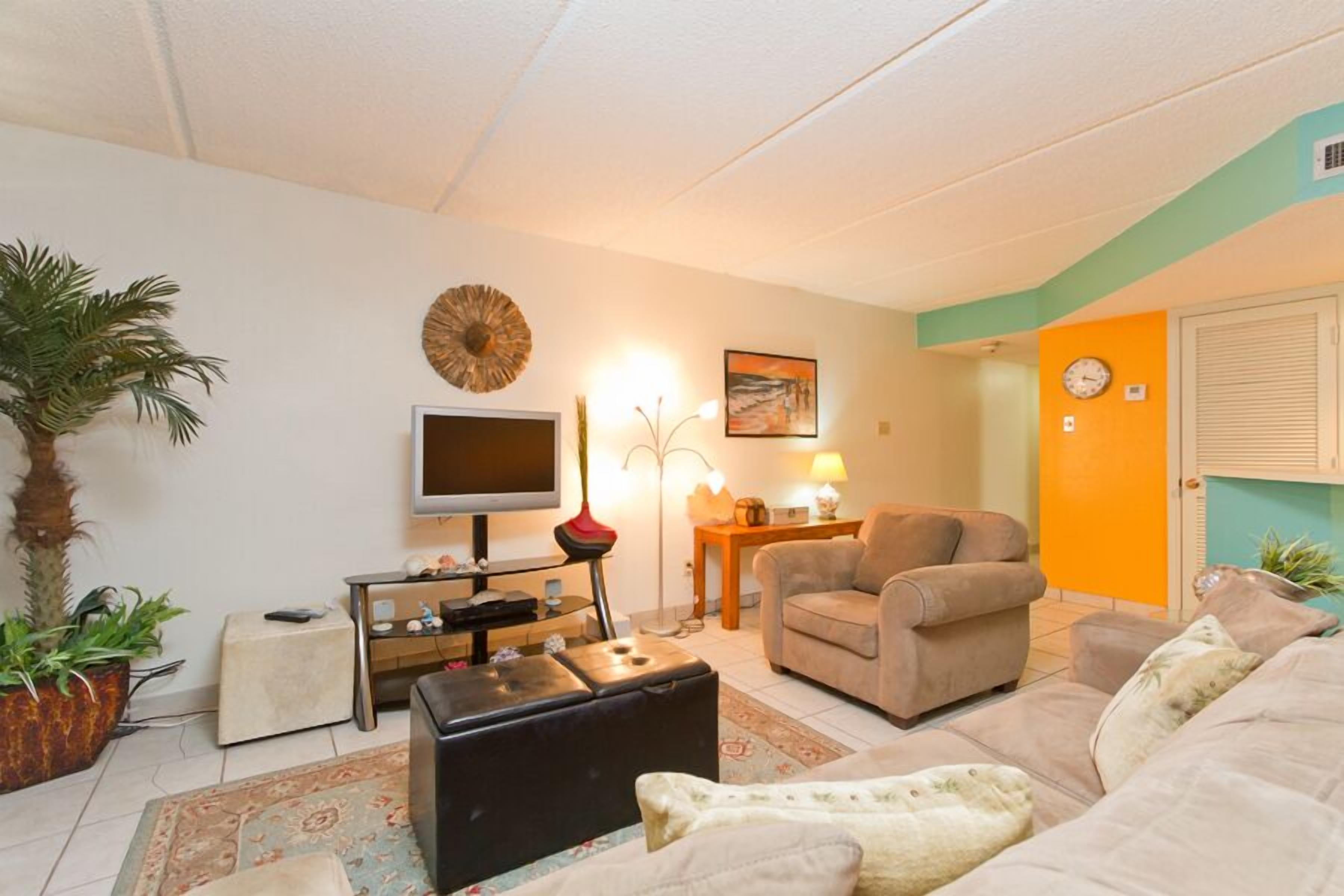 Una sala de estar con televisor, sofá, sillón, mesa de centro y plantas decorativas.