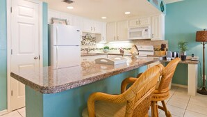 Una cocina con gabinetes blancos, encimera de granito y taburetes de mimbre.