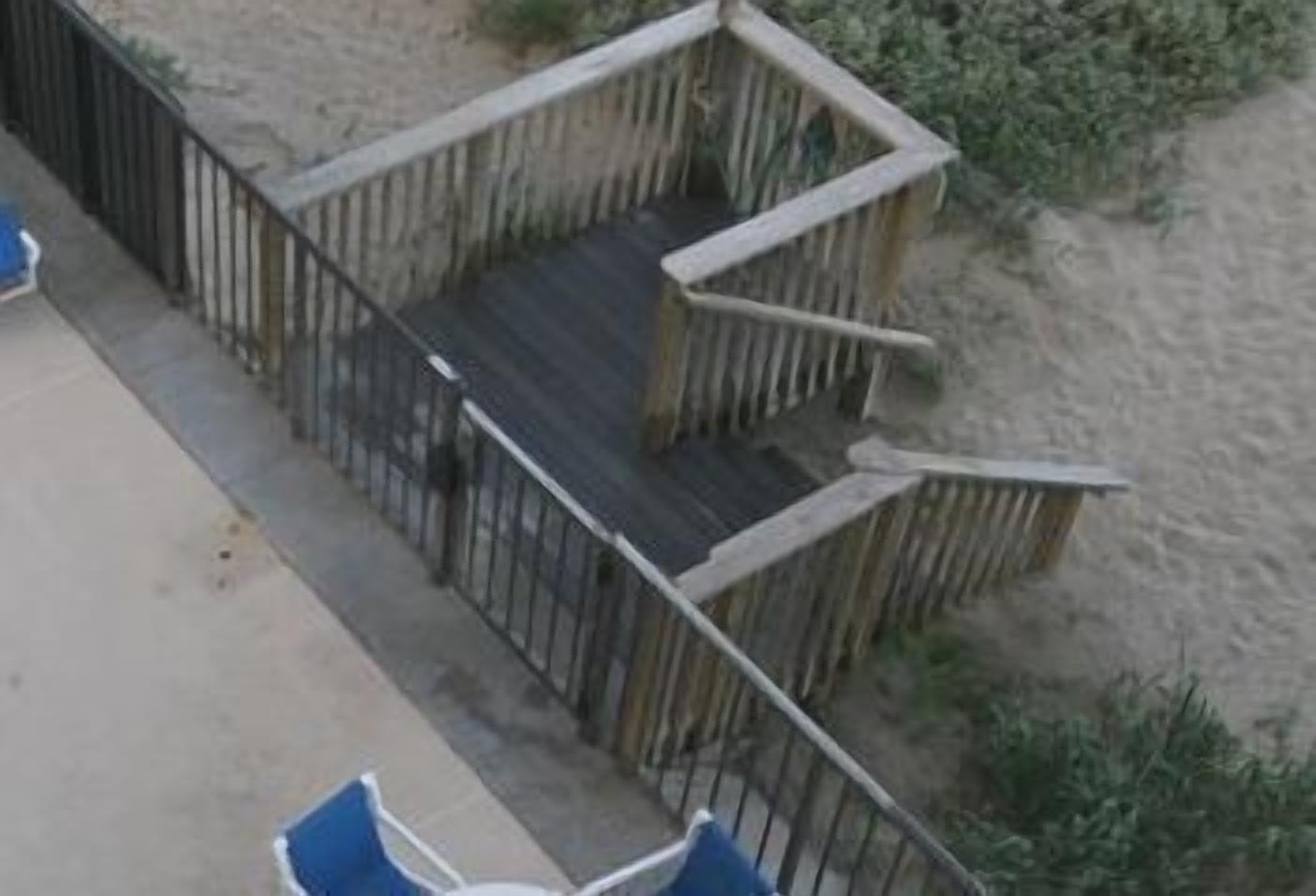 Eine Holzterrasse mit Geländer, einem Betonboden und einigen blauen Stühlen.