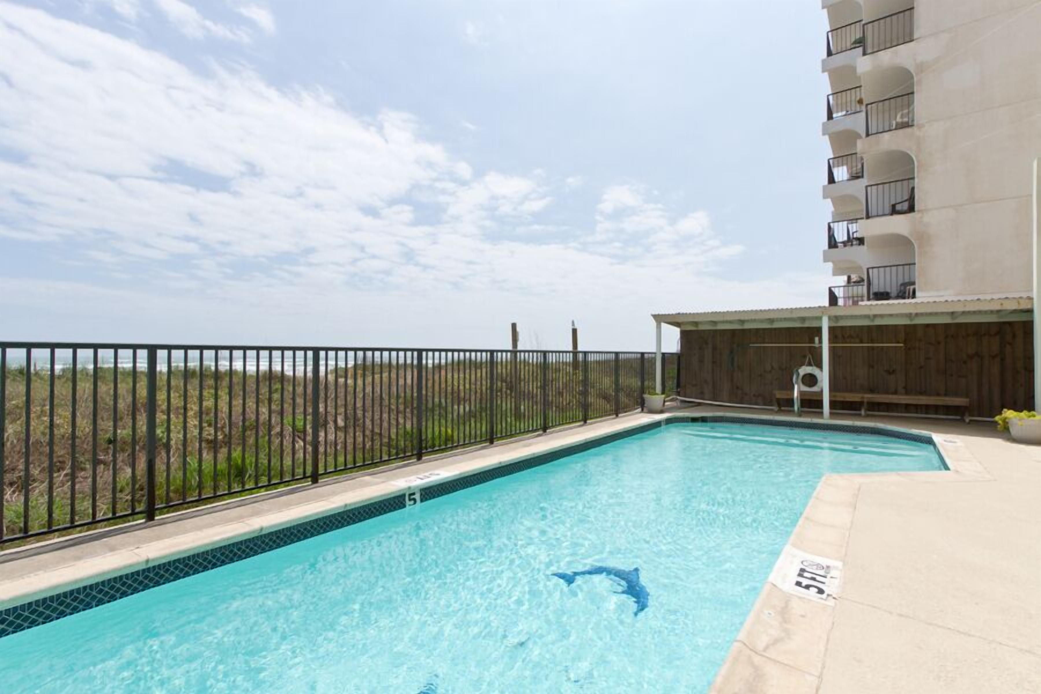 A swimming pool with a dolphin decal, surrounded by a black fence, and a building with balconies in the background.