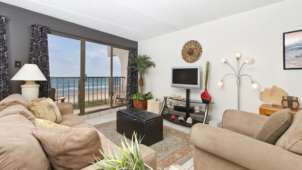Sala de estar con sofá, mesa de centro, televisor y planta. Balcón con vistas al mar.