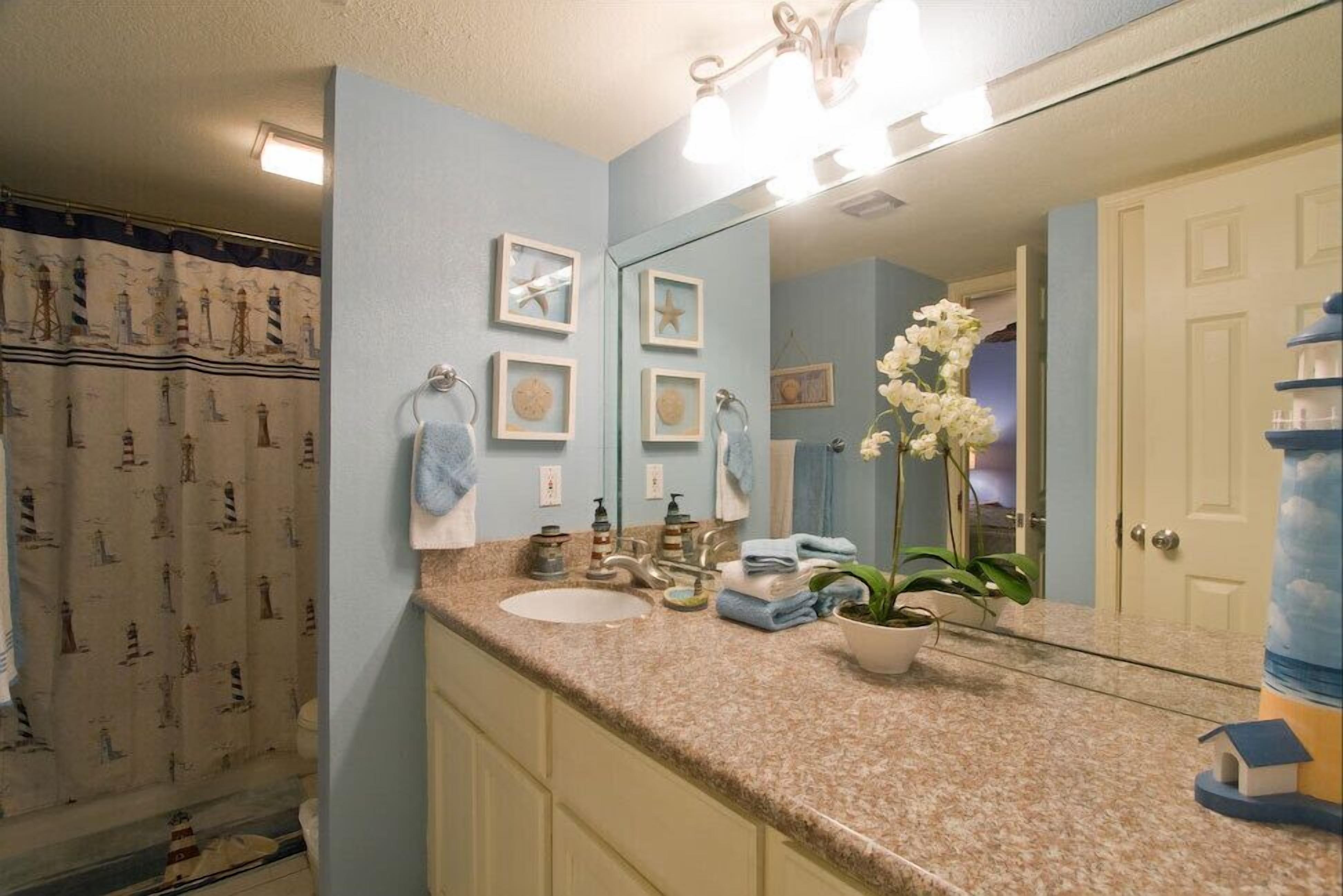 A bathroom with a sink, mirror, and towel rack. There is a shower curtain with a lighthouse pattern.