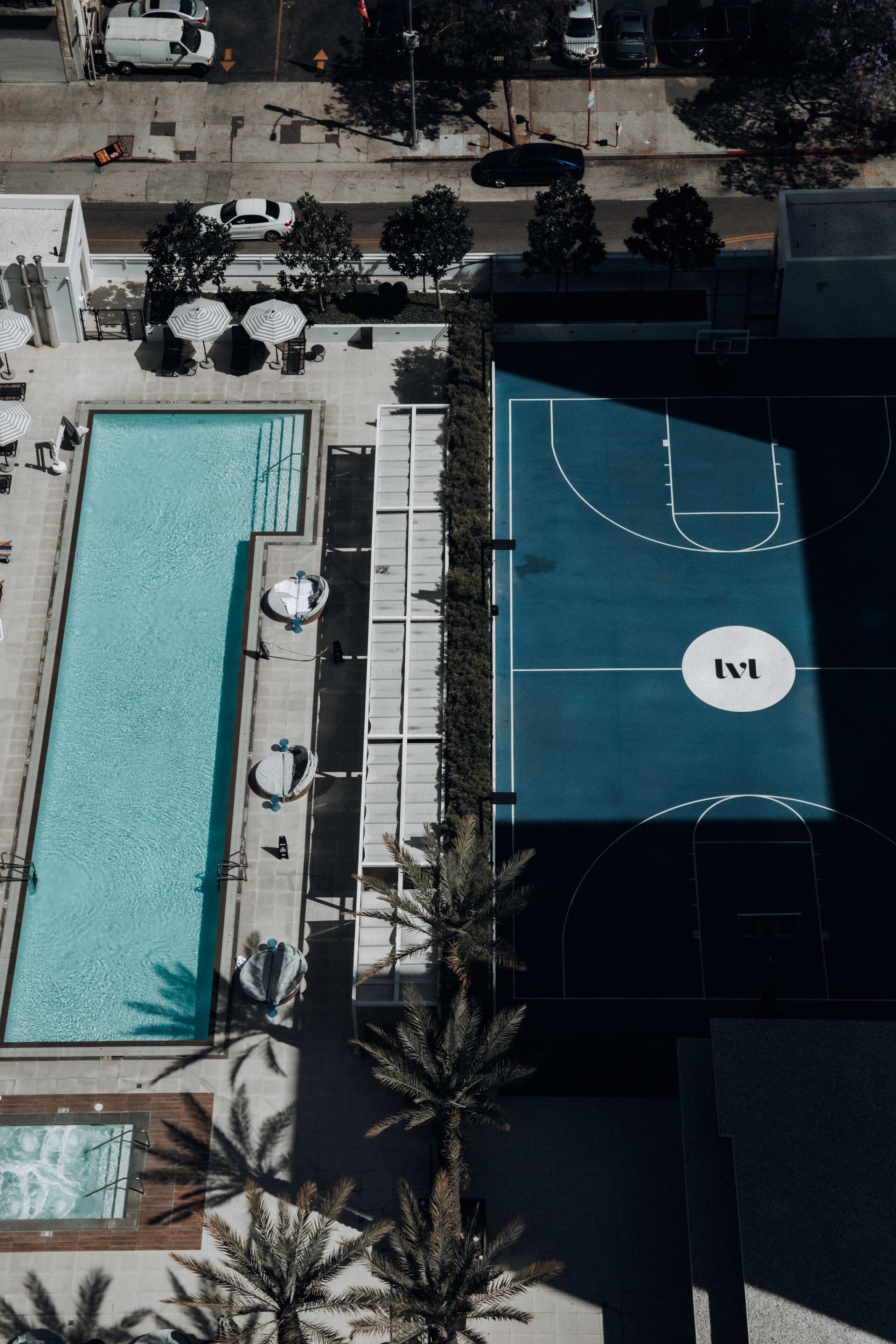 An aerial view of a hotel with a swimming pool, sun loungers, and a basketball court.