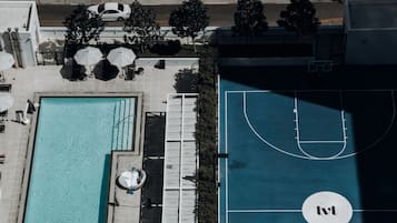 Una vista aerea di un hotel con piscina, lettini prendisole e campo da basket.