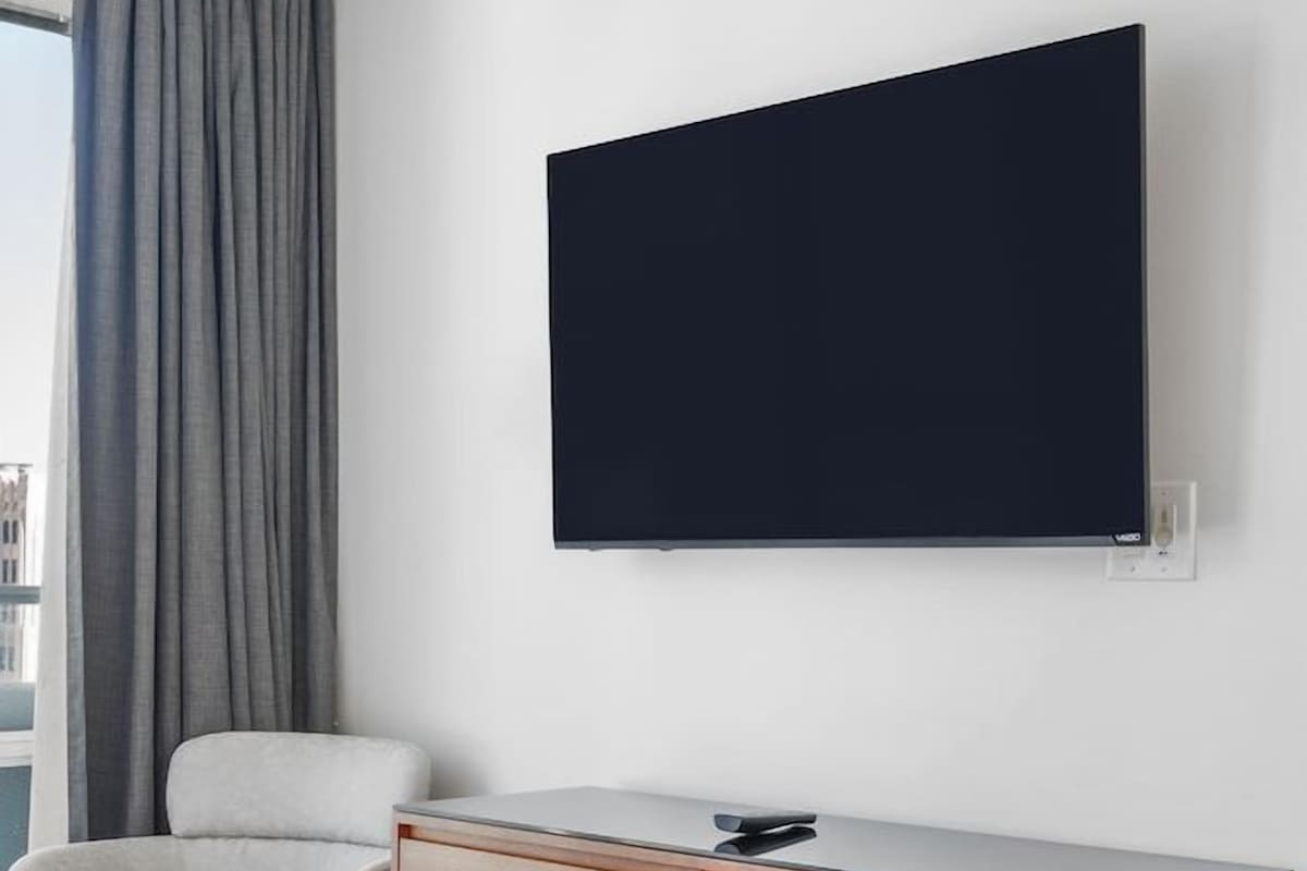 Moderni hotellihuone, jossa on suuri sänky, puinen työpöytä, tuoli ja seinälle asennettu litteänäyttöinen televisio.