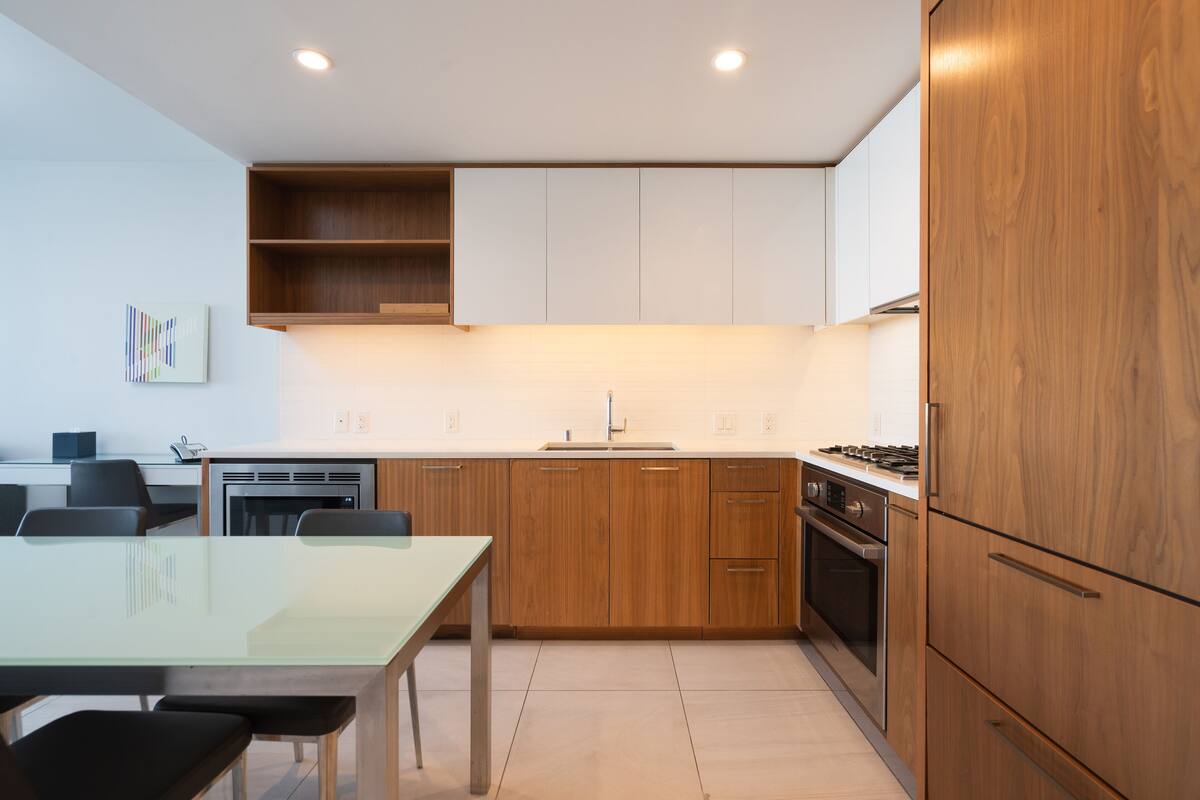 Een moderne keuken met houten kastjes, een roestvrijstalen fornuis en een glazen eettafel.