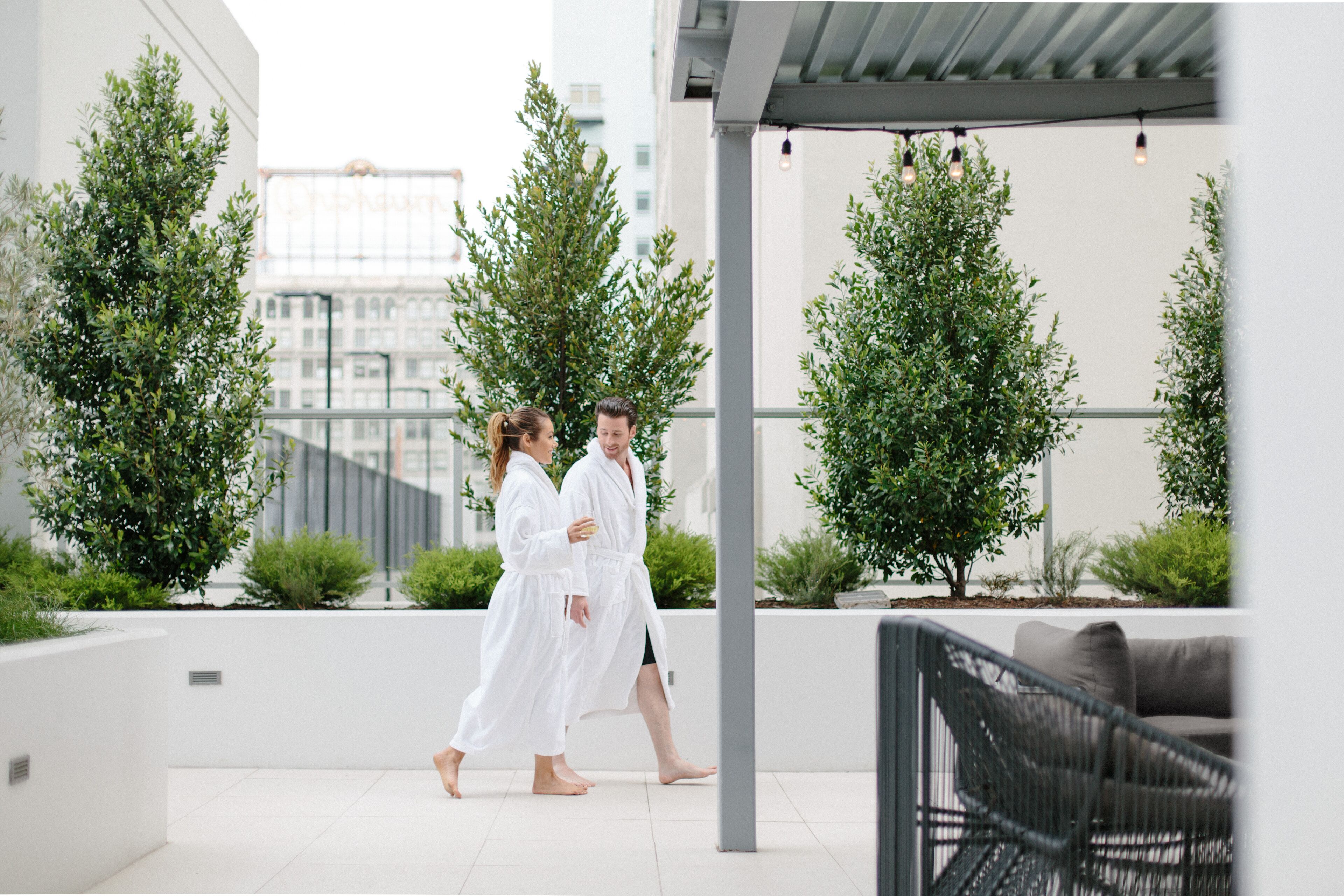 A modern outdoor area with a white wall, potted plants, and a black wicker chair.