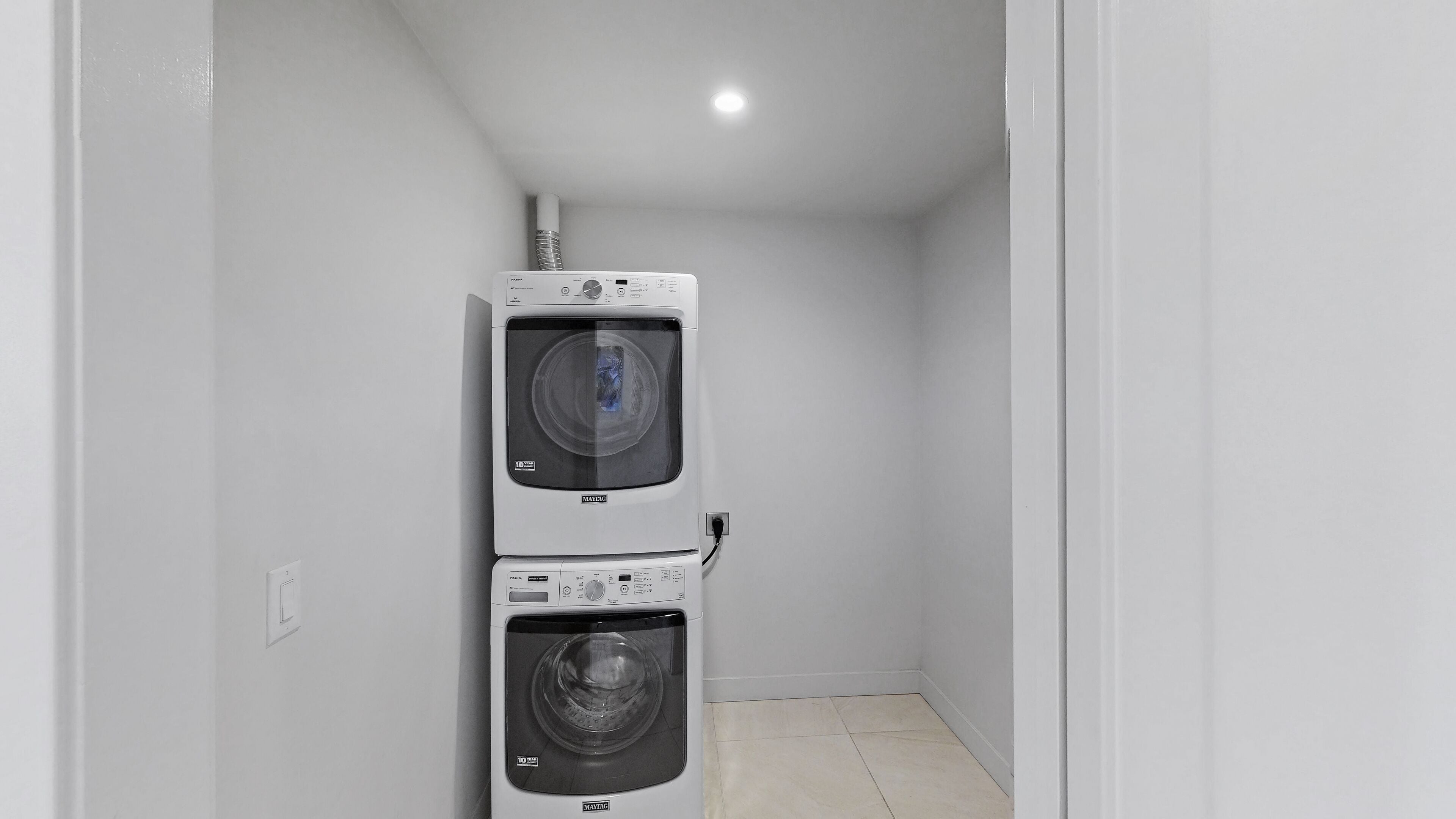 A compact laundry room with two stacked washing machines, a visible power outlet, and a light fixture on the ceiling.