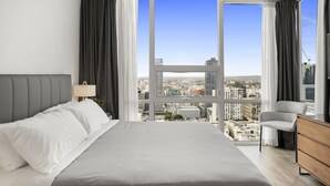 Une chambre d’hôtel moderne, dotée d’un grand lit, offrant une vue sur la ville et permettant d’admirer le paysage urbain à travers les fenêtres.