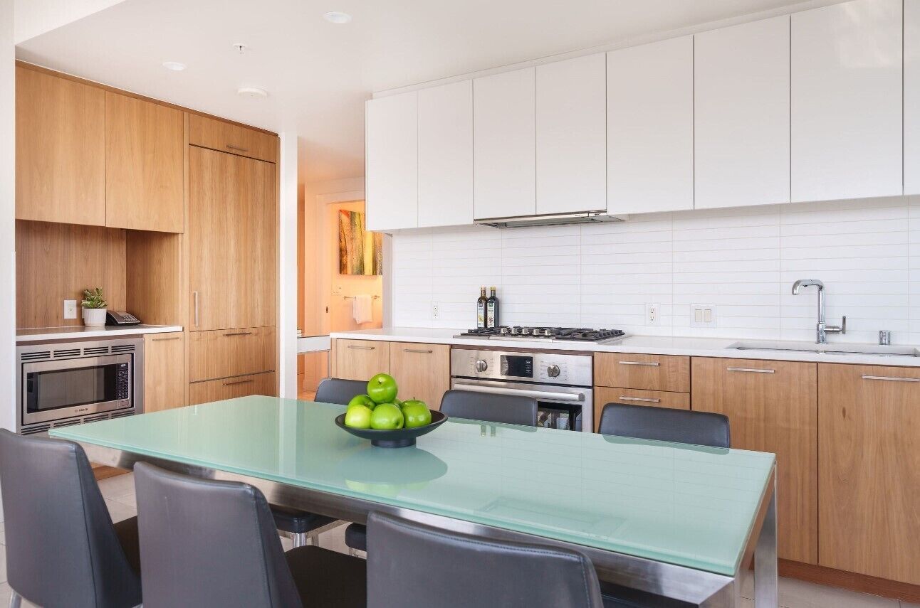 Una cocina moderna con armarios blancos, una mesa de comedor de vidrio y un tazón de manzanas verdes.