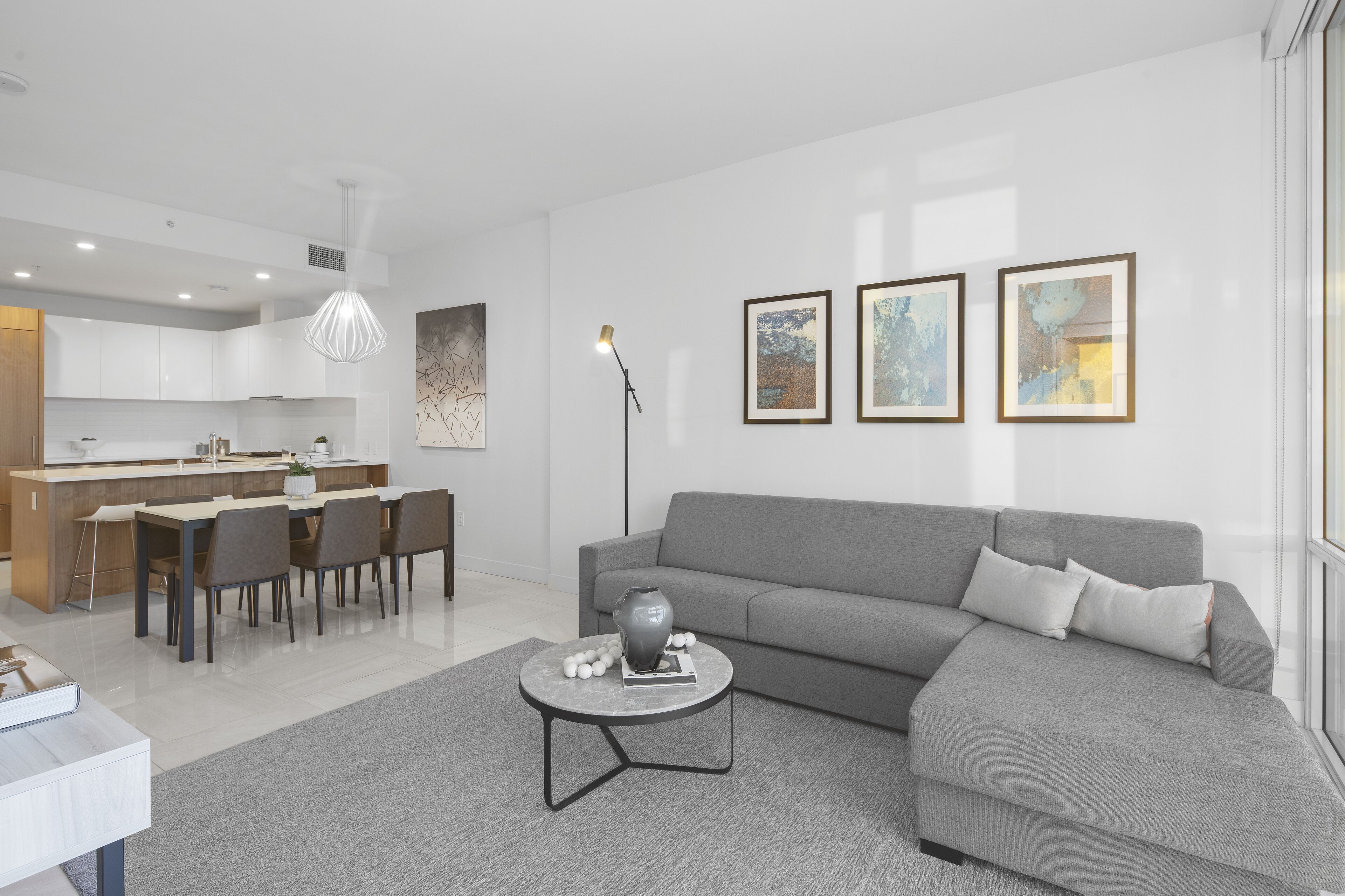 A modern living room with a grey sofa, a round coffee table, and a dining area with a kitchen in the background.
