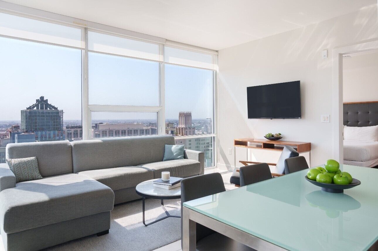 A modern living room with a sofa, a dining table, and a TV on the wall.