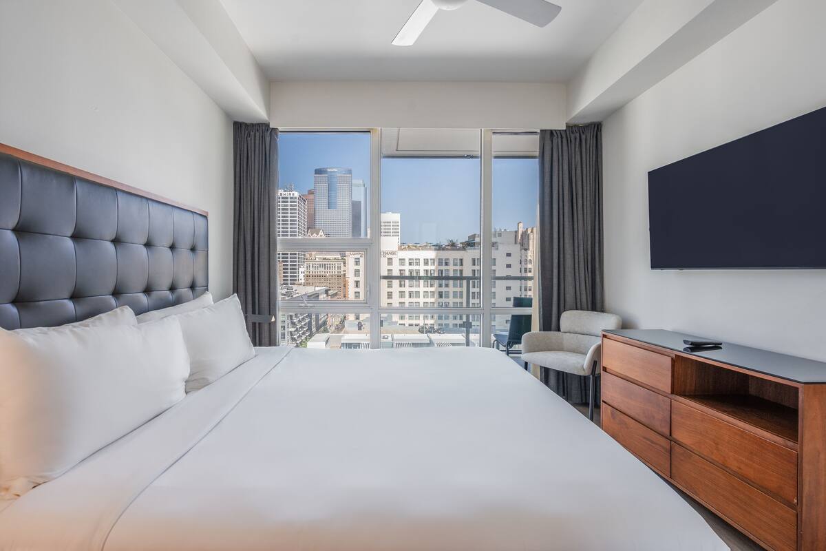 Een hotelkamer met een groot bed, een houten dressoir, een stoel en een televisie aan de muur.