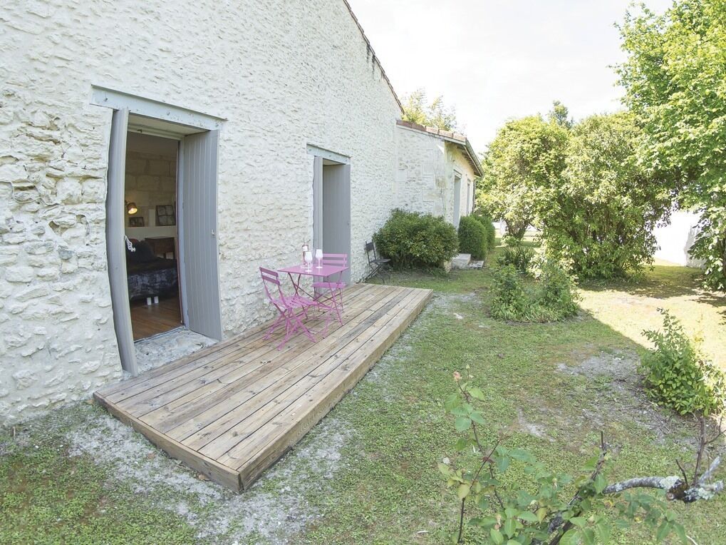 En rustik bygning i sten med en træterrasse og en pink stol.