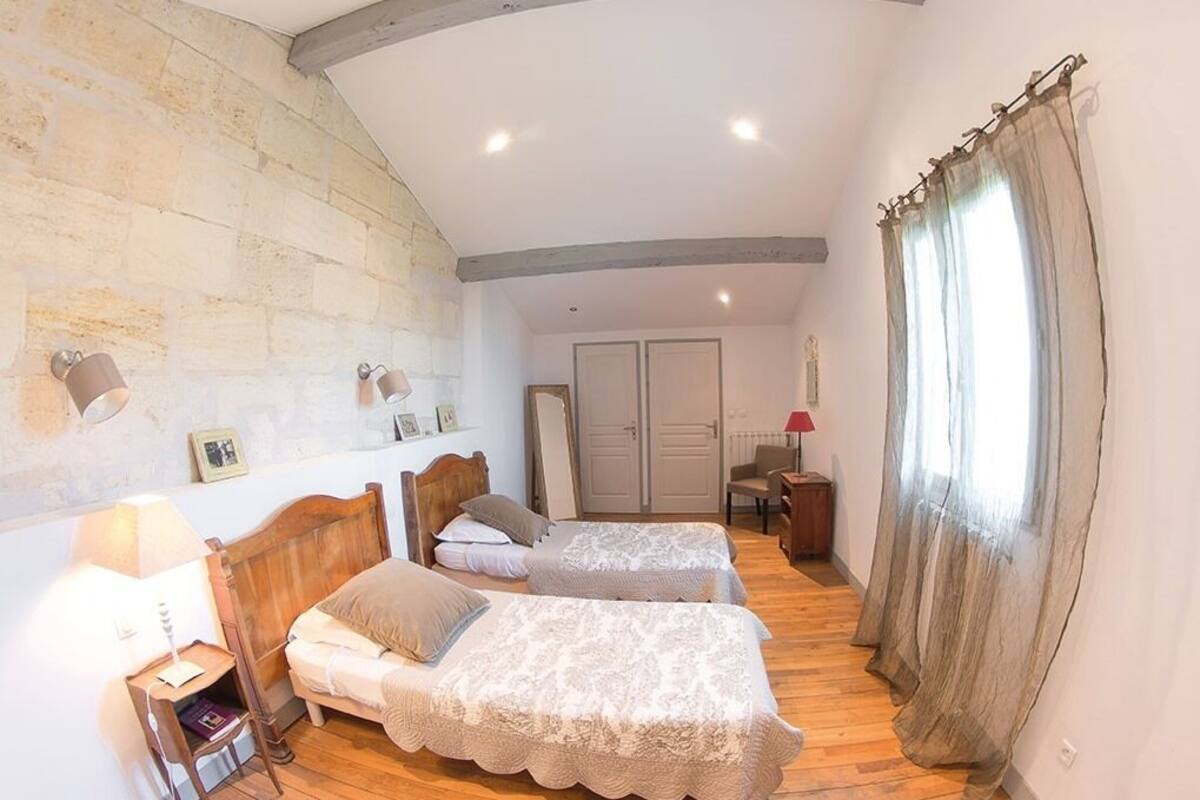 A bedroom with two beds, a wooden floor, a stone wall, and a ceiling with exposed beams.