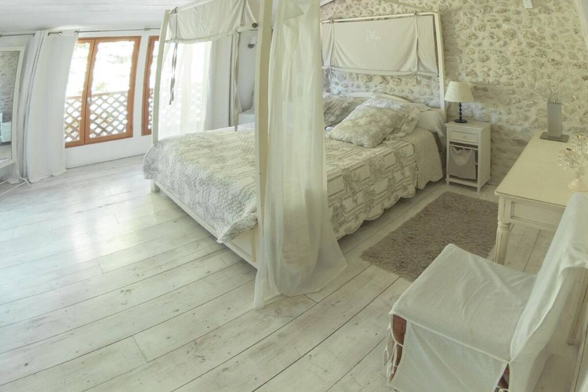 A bedroom with a four-poster bed, a nightstand, and a desk with a lamp.