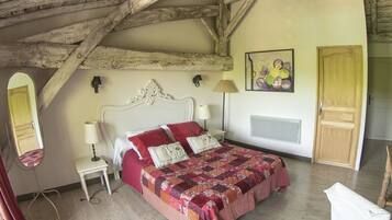 Une chambre à coucher avec un plafond en bois, un lit recouvert d’une couette rouge et blanche, une table de chevet avec une lampe, une œuvre d’art accrochée au mur et une porte.