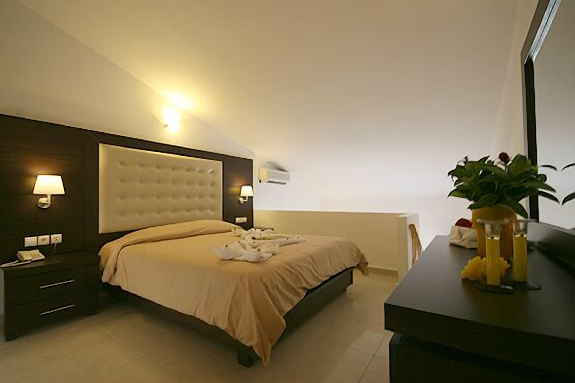 Quarto de hotel com uma cama grande, abajures, mesa de cabeceira, escrivaninha com uma planta e uma janela.