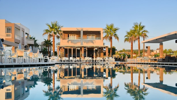 Un hotel con piscina, mobiliario exterior y palmeras.