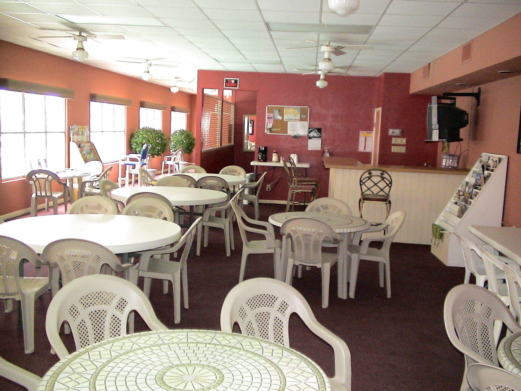 A dining area with multiple tables and chairs, a bulletin board, and ceiling fans.