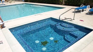 A swimming pool with a small section of a hot tub, surrounded by lounge chairs and a tiled deck.