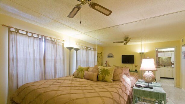 A bedroom with a large bed, a ceiling fan, a nightstand with a lamp, and a mirror.