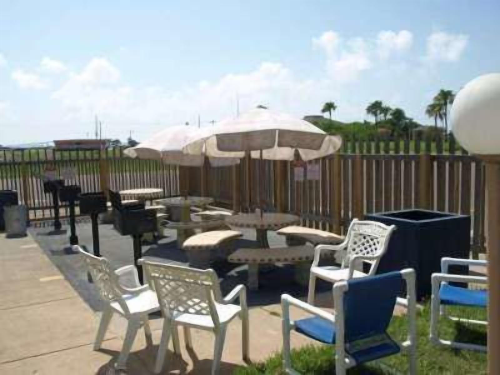 An outdoor patio area with white and blue chairs, a round table, and two umbrellas.