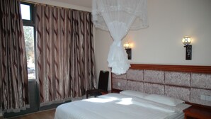 A bedroom with a large bed, a wooden headboard, two wall-mounted lights, and a window with curtains. - Golden Chopstick Hotel (Livingstone)