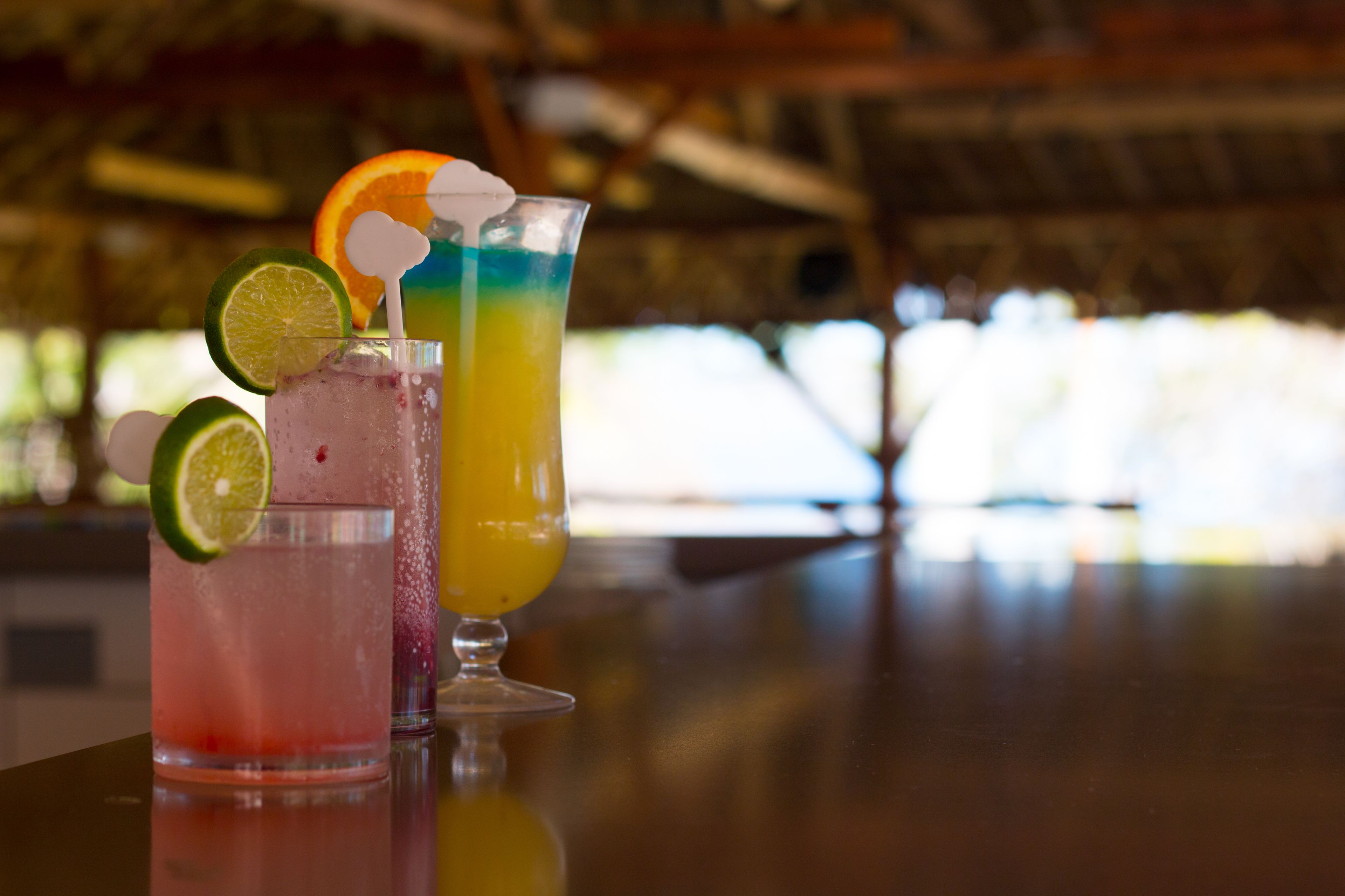 Drie kleurrijke cocktails op een bar met een onscherpe achtergrond.