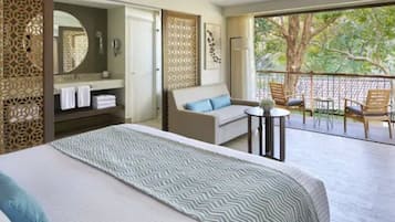 A hotel room with a bed, a sofa, a small table, and a balcony with chairs.