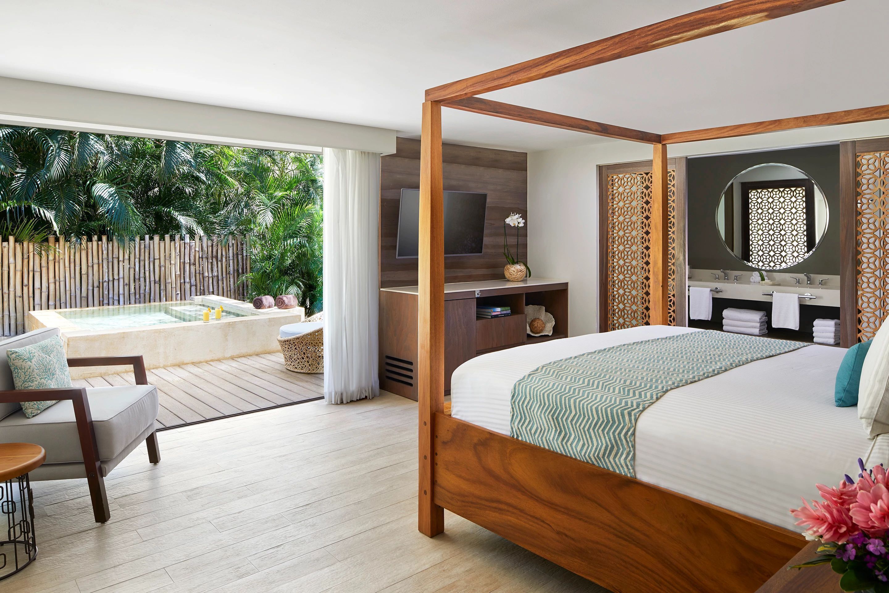 Une chambre spacieuse dotée d’un grand lit, d’une télévision, d’une coiffeuse avec un miroir et offrant une vue sur un espace extérieur privé agrémenté d’un jacuzzi.