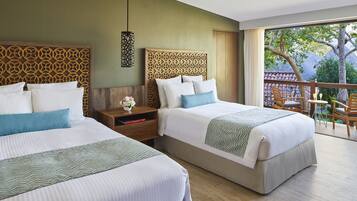 A hotel room with two beds, a nightstand with a vase of flowers, and a balcony with chairs and a table.