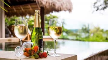 Une bouteille de champagne, deux verres de vin blanc et un verre garni de fraises, posés sur le bord d’une piscine.
