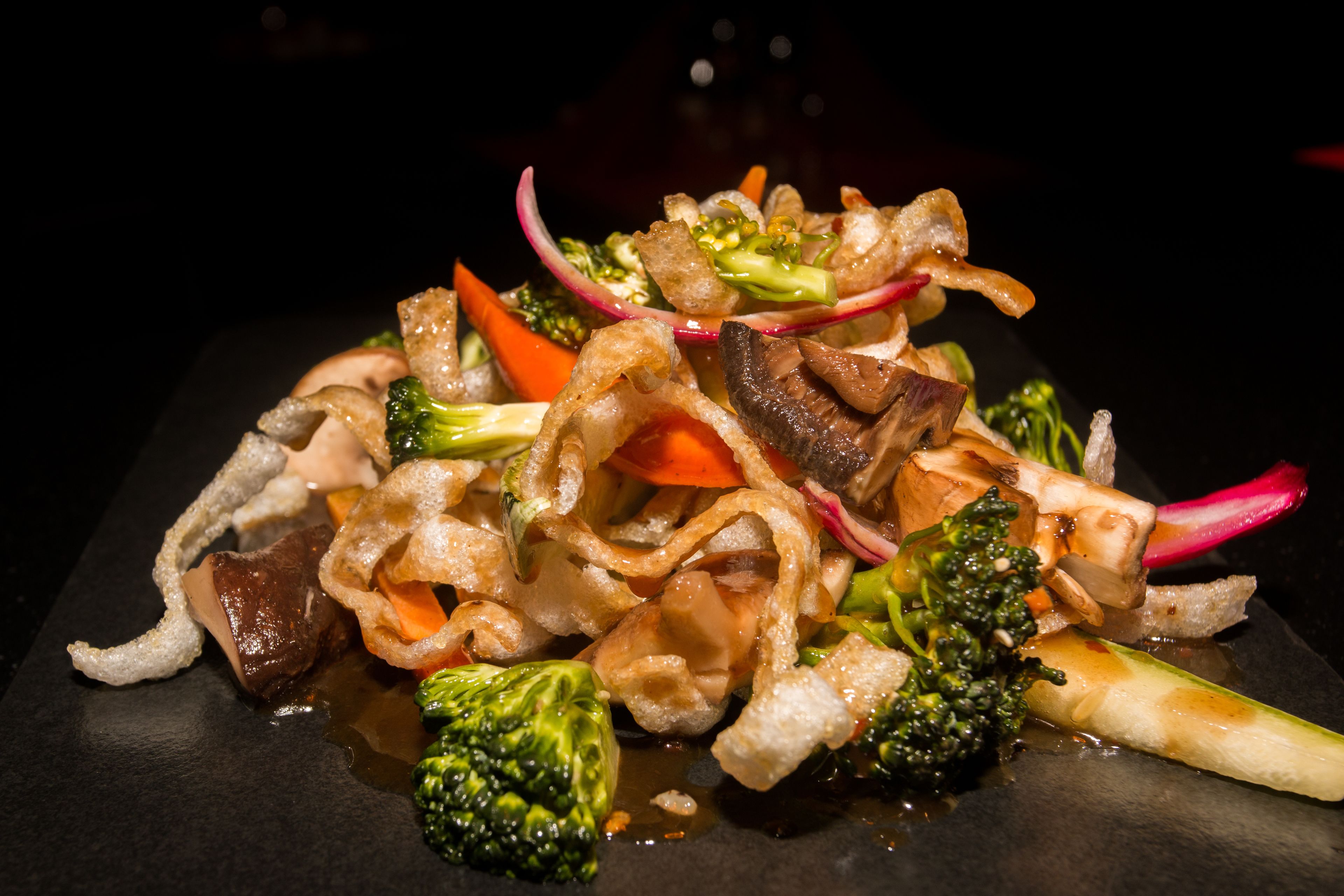 A dish with various vegetables and meat, served on a dark plate.