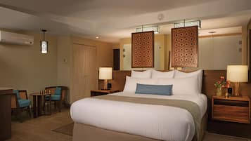 Una habitación de hotel con una cama grande, dos mesitas de noche con lámparas, una pequeña mesa con sillas y un separador decorativo.