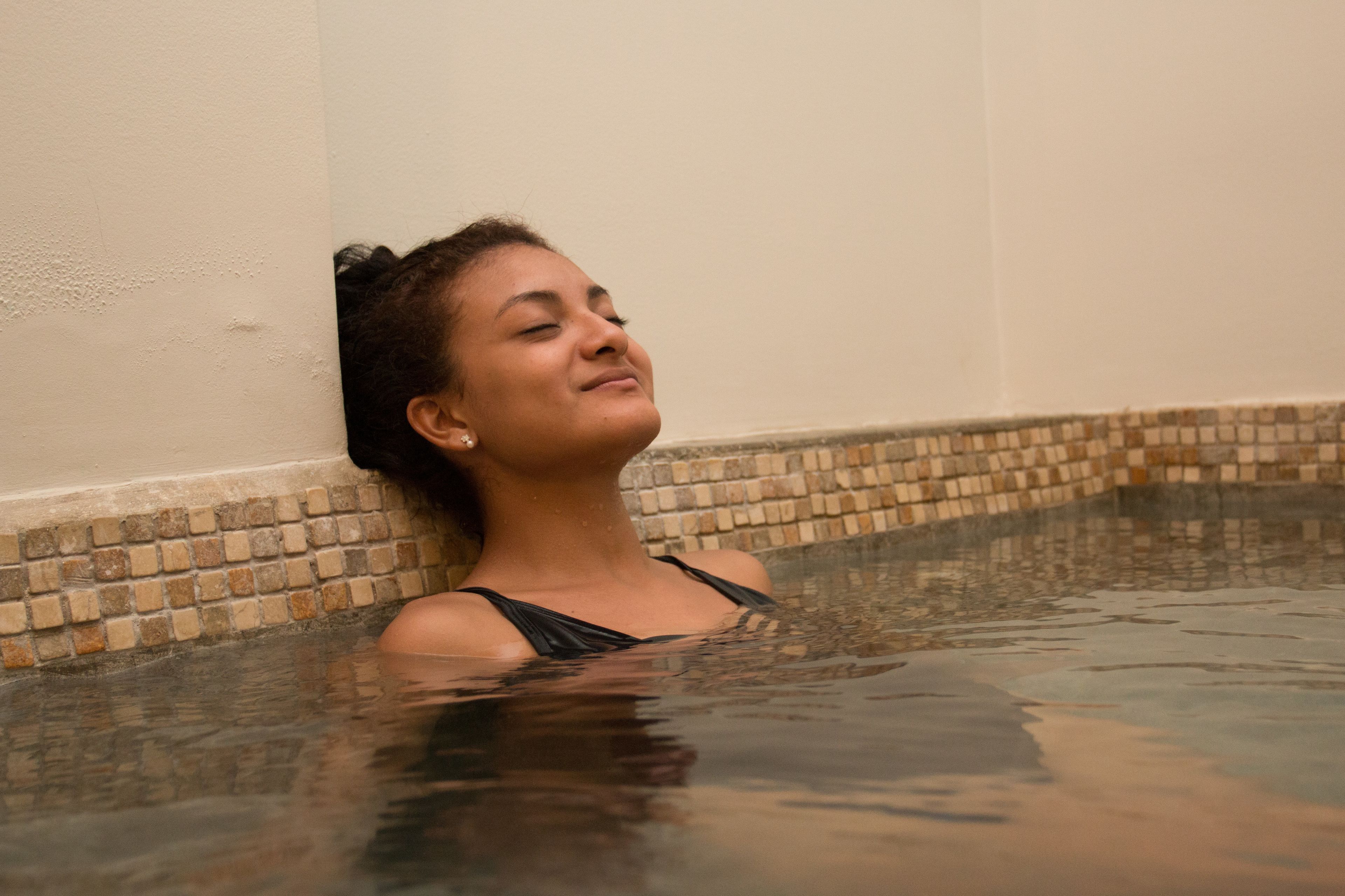 A person in a hot tub with a tiled wall and a tiled floor.