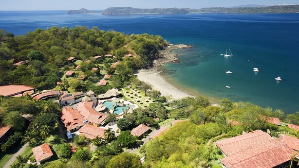 Une vue aérienne d’une station balnéaire avec de nombreux bâtiments, une plage et des bateaux sur l’eau.