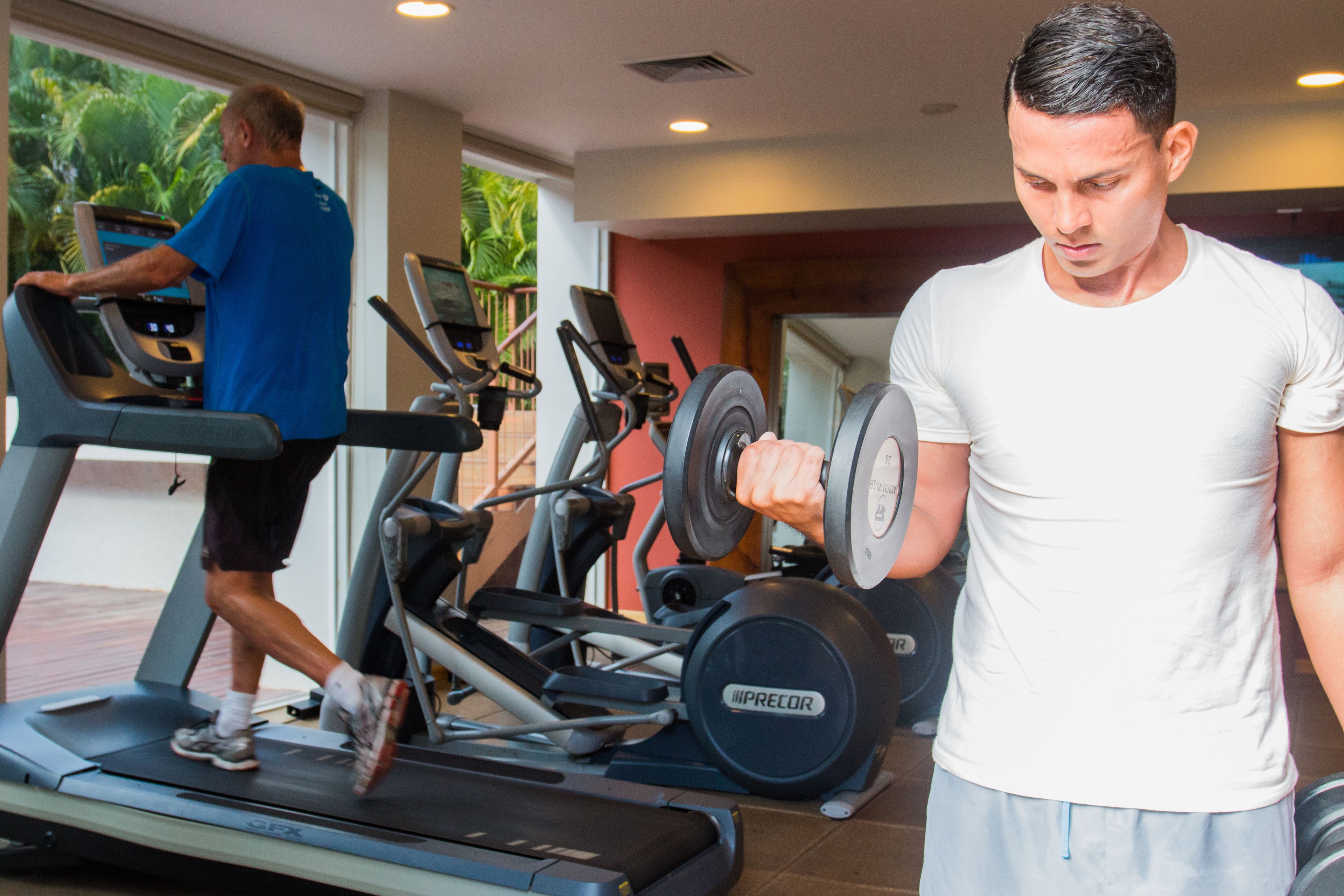 A gym with treadmills, a man lifting weights, and another using a treadmill.