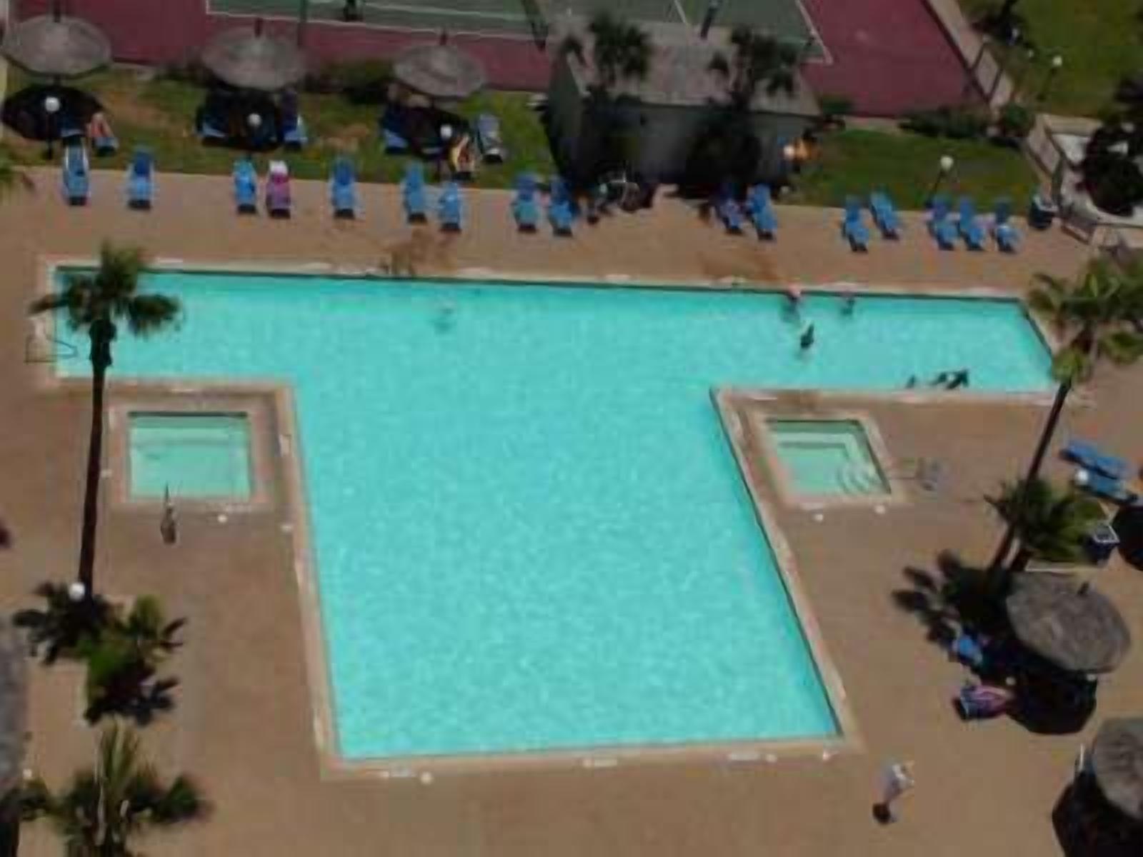 Una grande piscina rettangolare con superficie dell'acqua limpida e blu, circondata da lettini e ombrelloni.