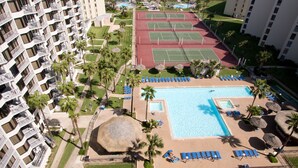 A hotel with multiple floors, a swimming pool, tennis courts, and palm trees. - Saida by South Padre Condo Rentals (South Padre Island)