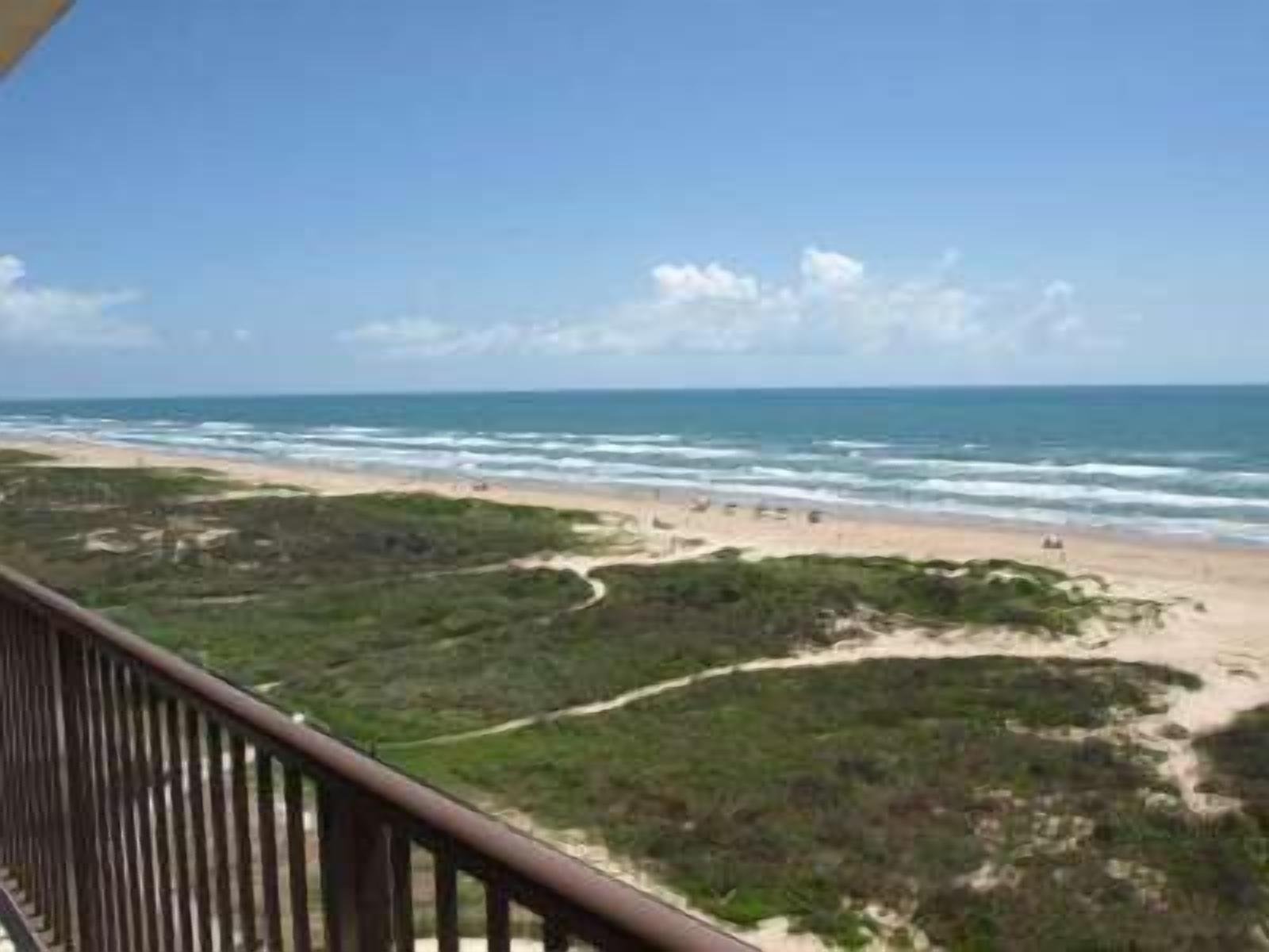 A beach view from a balcony with a railing, sandy beach, and ocean.