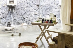 Un área de spa con pared de piedra, fuente de agua y una mesa con varias botellas y un tazón.