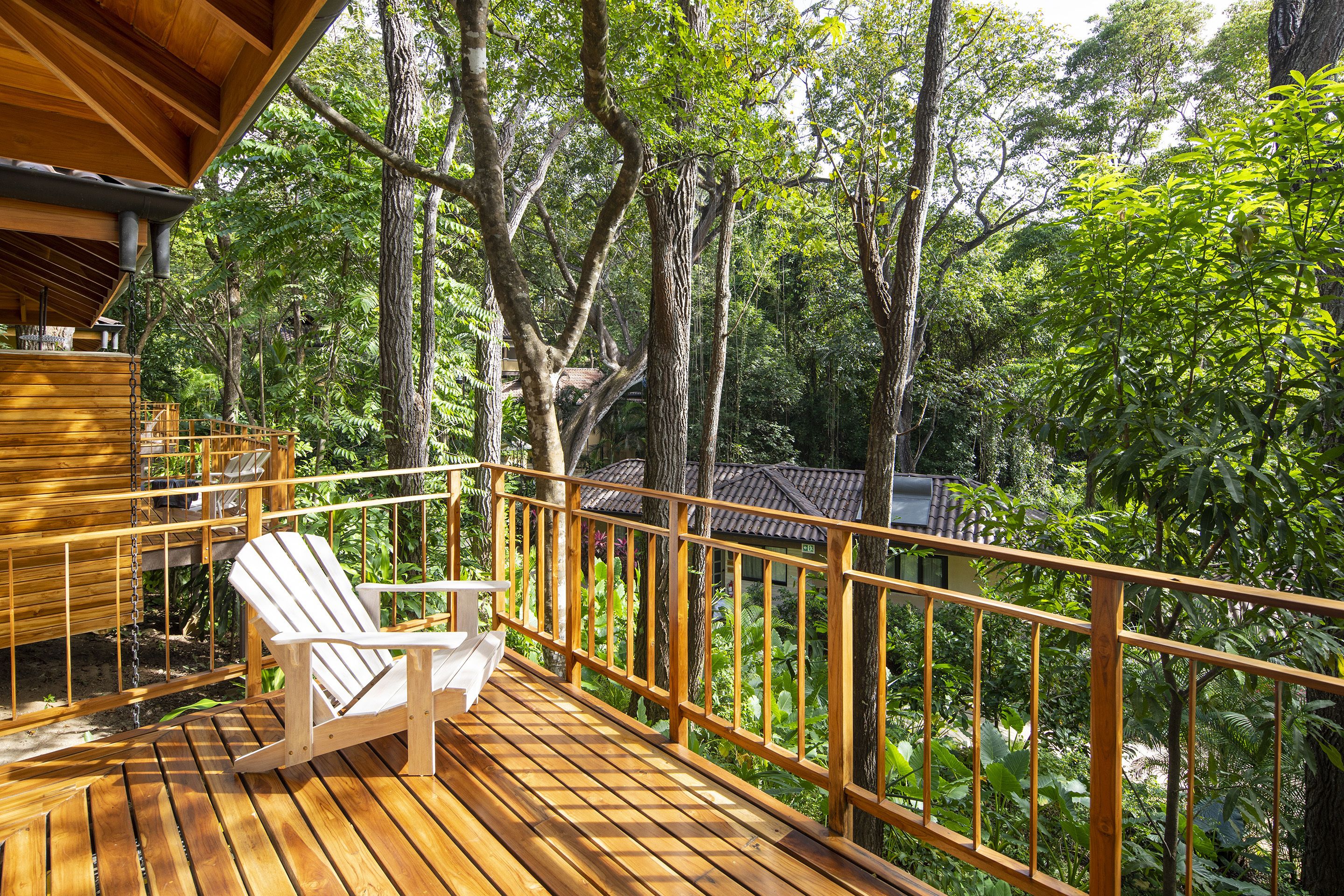 A wooden deck with a white chair, surrounded by dense foliage and trees.