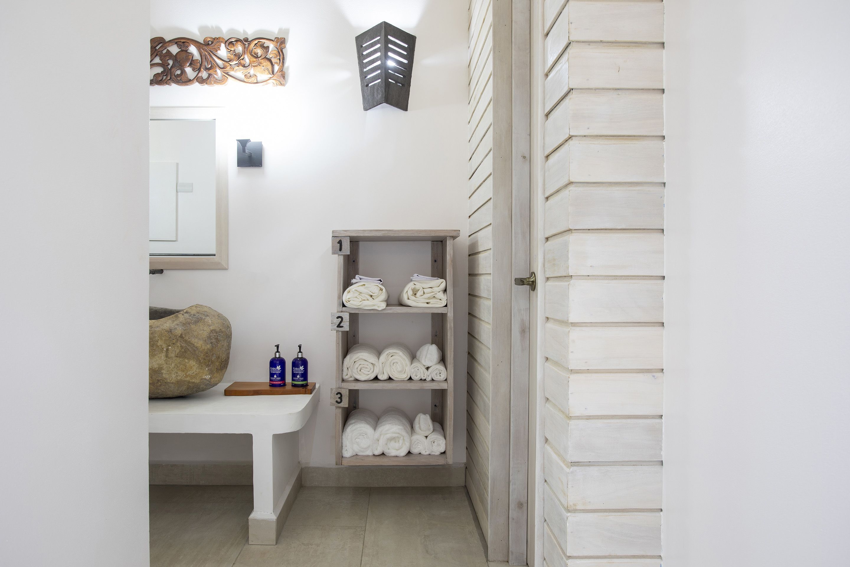 Un baño con un banco de madera, un perchero con toallas y un dispensador de jabón.