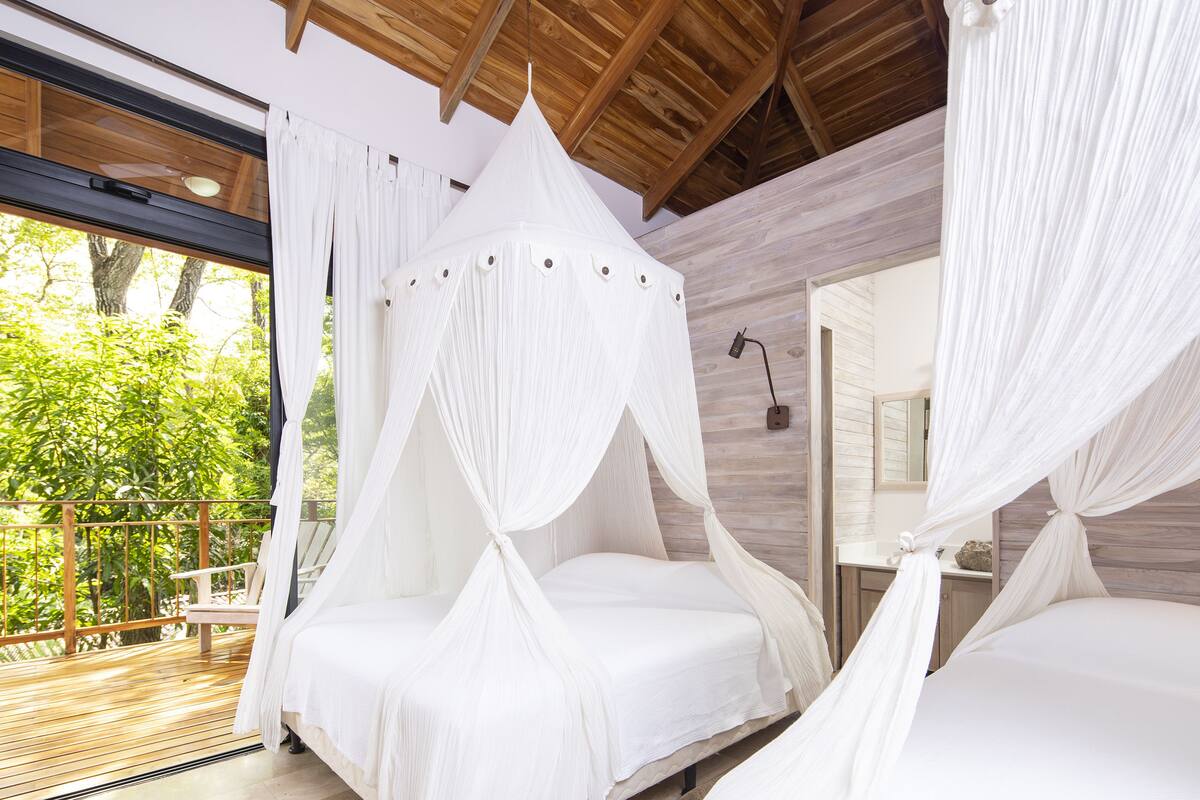 Une chambre à coucher avec un lit à baldaquin, un plafond en bois et une vue sur la verdure environnante.