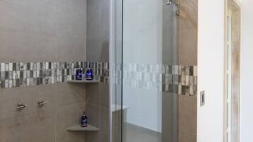 A modern shower area with a glass door, a tiled shower floor, and a shelf with toiletries.