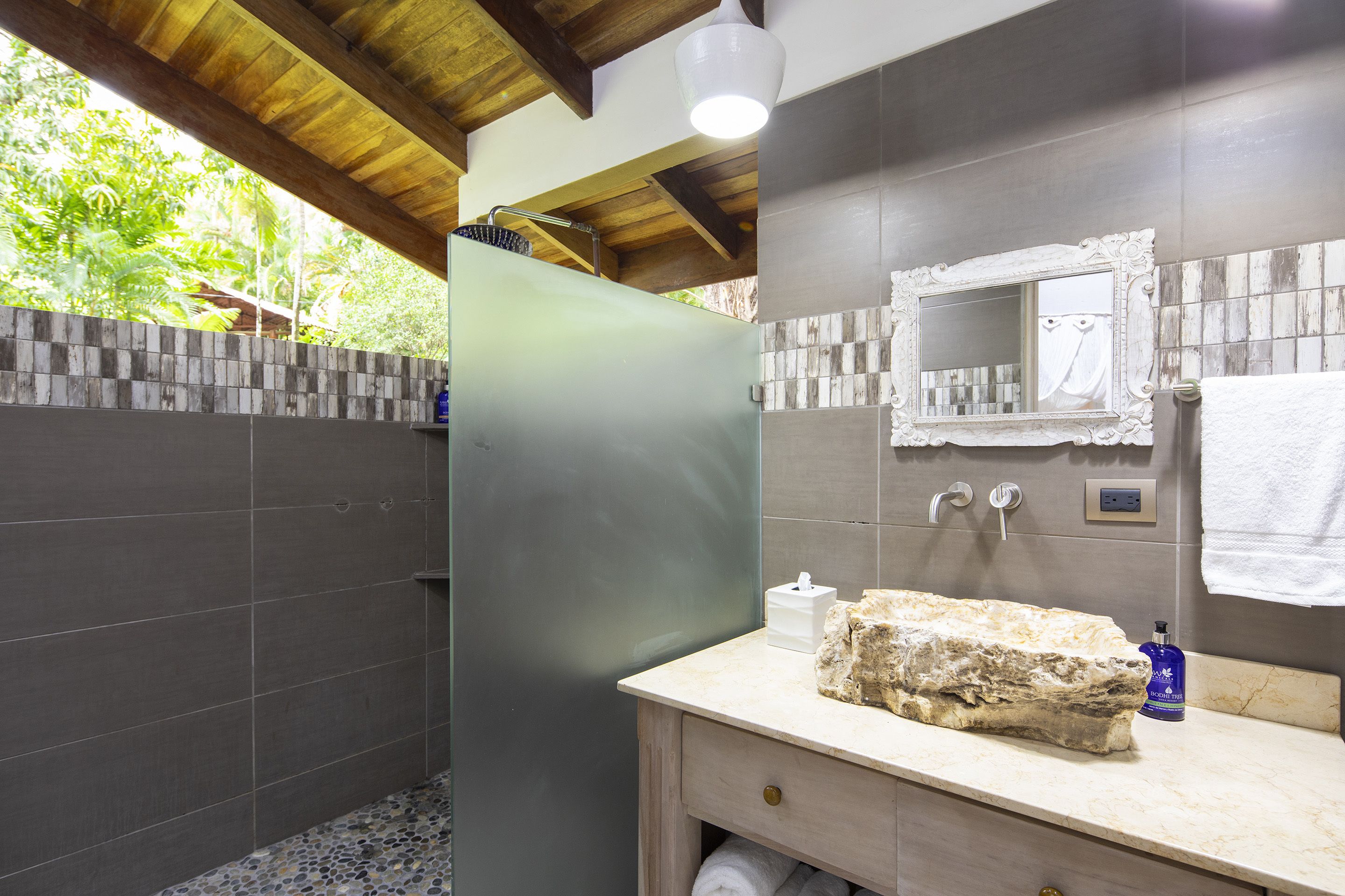 A bathroom with a shower, a sink with a stone basin, a mirror, and a towel hanging on the wall.