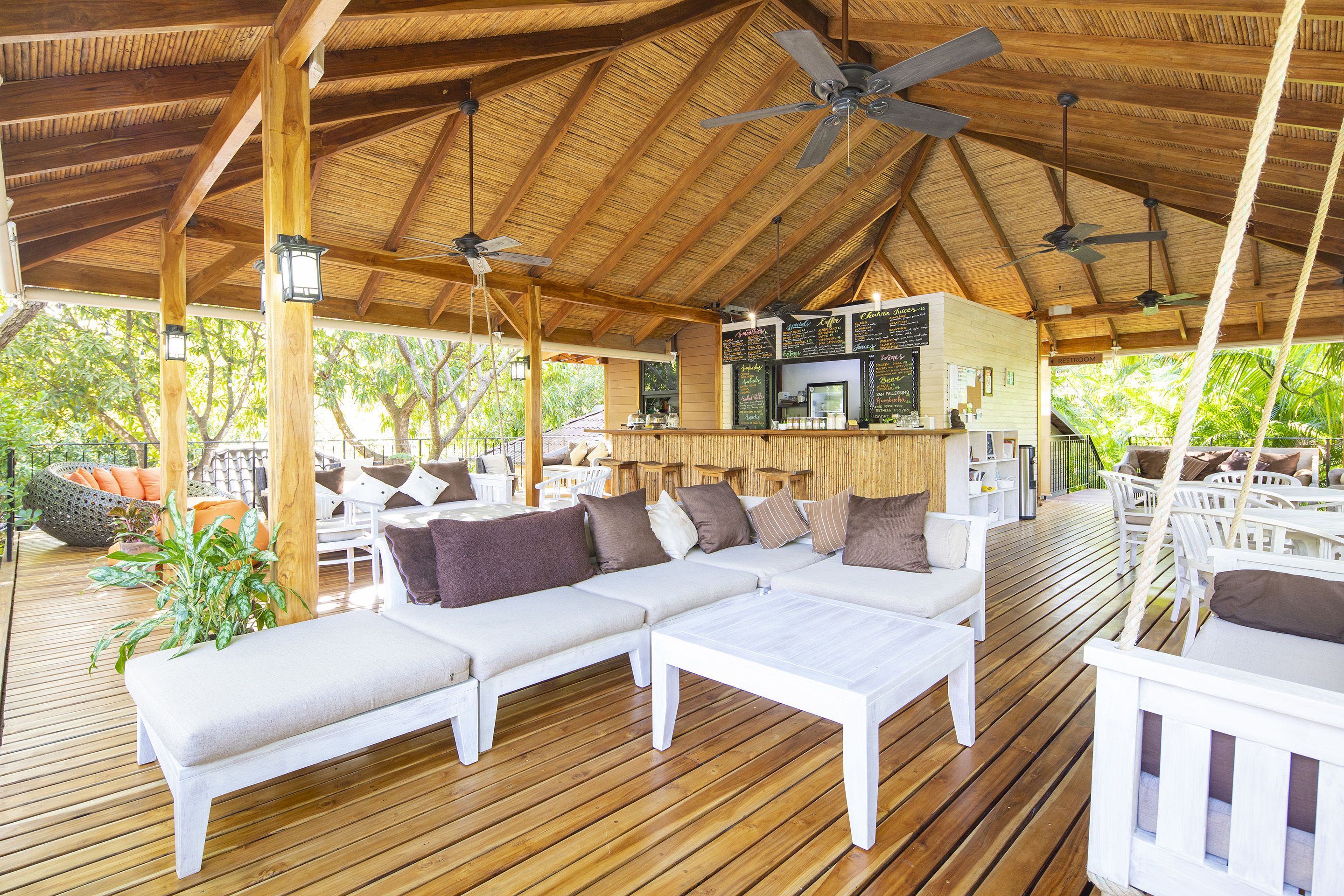 Area relax esterna coperta con pavimento in legno, mobili bianchi e ventilatori a soffitto.