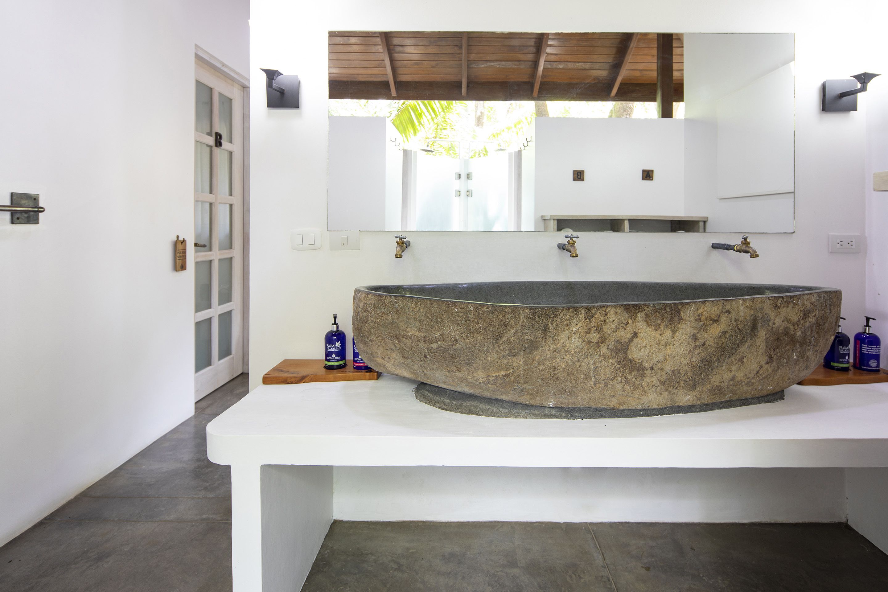 A bathroom with a large stone sink, a white countertop, and a large mirror above the sink.